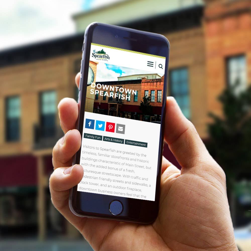 Visit Spearfish website on phone with a town background